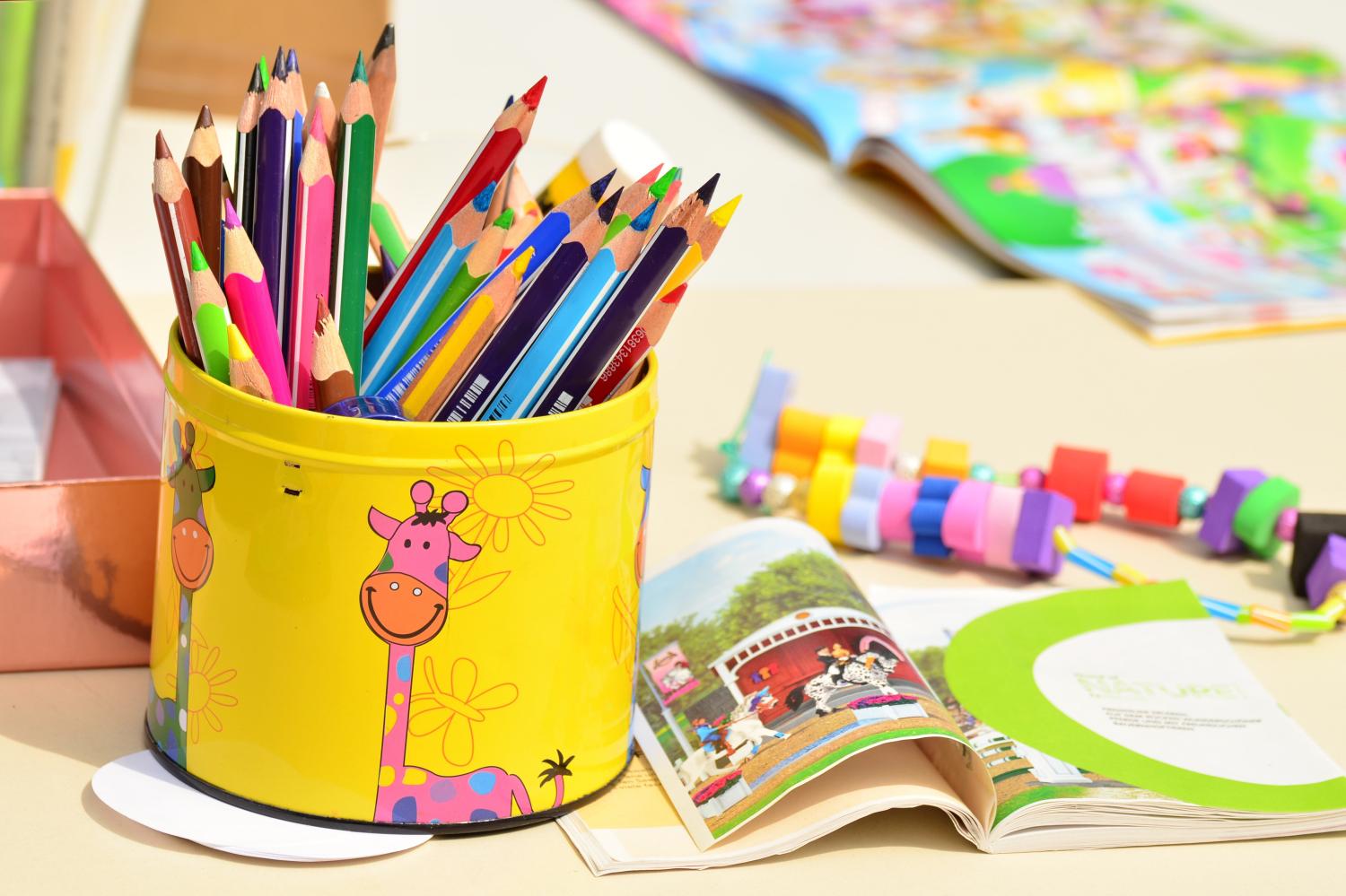 Bunte Stifte im gelben Becher mit Giraffenmotiv, daneben ein aufgeschlagenes Kinderbuch.